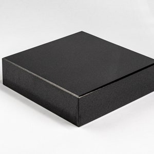 May include: A black square pedestal made of polished granite. The pedestal is about 12 inches wide and 4 inches tall.