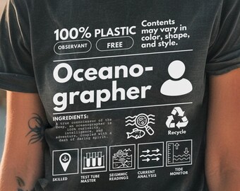 May include: A black t-shirt with white text that reads "100% PLASTIC OBSERVANT FREE Oceano-grapher" and includes a diagram of a person with a magnifying glass, a fish, a recycle symbol, a location pin, a test tube, a wave, an arrow, and a tide monitor. The text "Contents may vary in color, shape, and style." is also included on the shirt.