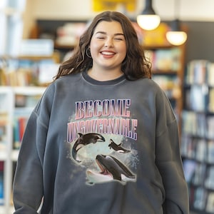May include: A dark grey sweatshirt with the text "BECOME UNGOVERNABLE" printed in pink and white. The sweatshirt features a graphic of three orcas jumping out of the water.
