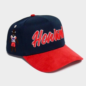 May include: Navy blue and red baseball cap with the word "Howard" in red script. The cap features a red brim and a small embroidered figure on the side.