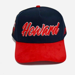 May include: A navy blue and red baseball cap with the name "Howard" embroidered in red script across the front. The cap has a red brim and a red button on top. The cap is a classic style.