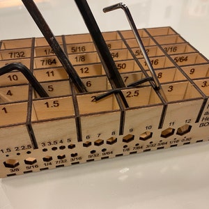 May include: A wooden organizer with a grid of compartments for storing hex keys. The organizer is labeled with both metric and imperial sizes, and includes the text "Millimeter and Inch Hex Key BOX".