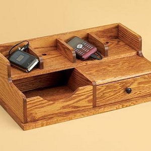 May include: Wooden organizer with a drawer and multiple compartments for storing small items like phones, chargers, and other electronics. The organizer is made of light brown wood with a natural finish.