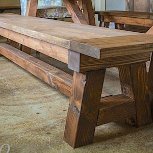 May include: A rustic wooden bench with a dark brown stain. The bench has a wide, flat top and a sturdy, A-frame base.