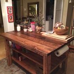 Puede incluir: Una isla de cocina de madera rústica con una encimera de madera marrón oscuro y estantes abiertos. La isla tiene un porta rollo de papel sujeto al lado.