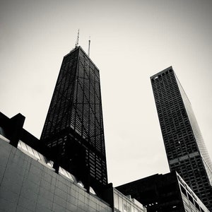 Può includere: Una fotografia in bianco e nero di due grattacieli alti in una città. Gli edifici sono moderni e hanno un design elegante. La foto è scattata da un angolo basso, guardando verso l'alto gli edifici.