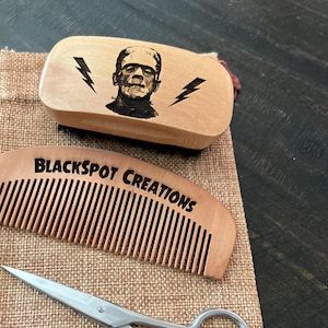 May include: A wooden comb, a wooden brush with a Frankenstein image, and a pair of silver scissors are displayed on a brown burlap bag. The brush has the text "Blackspot Creations" on it.