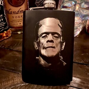 May include: Black metal flask with a silver top and a black and white image of Frankenstein's monster on the front.