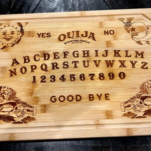 May include: A wooden cutting board with an engraved Ouija board design. The board features the letters A through Z, numbers 0 through 9, and the words "YES", "NO", "GOOD BYE", and "OUIJA MYSTIFYING ORACLE".
