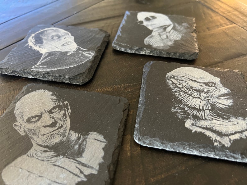 May include: Four black slate coasters with white etched images of classic horror movie monsters. The coasters feature the Creature from the Black Lagoon, the Mummy, Frankenstein's Monster, and the Wolfman.