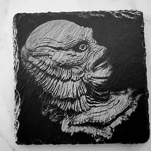 May include: Black and white image of a creature from the black lagoon on a slate coaster.