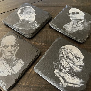 May include: Four black slate coasters with white images of classic horror movie monsters. The coasters feature the Creature from the Black Lagoon, the Invisible Man, the Wolfman, and the Mummy.