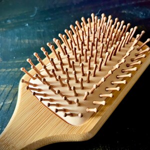May include: A wooden hairbrush with a rectangular head and a handle. The brush features numerous wooden bristles with rounded tips. The wood has a light brown color, and the bristles are a similar shade.