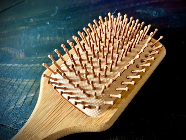 May include: A wooden hairbrush with a rectangular head and a handle. The brush features numerous wooden bristles with rounded tips. The wood has a light brown color, and the bristles are a similar shade.
