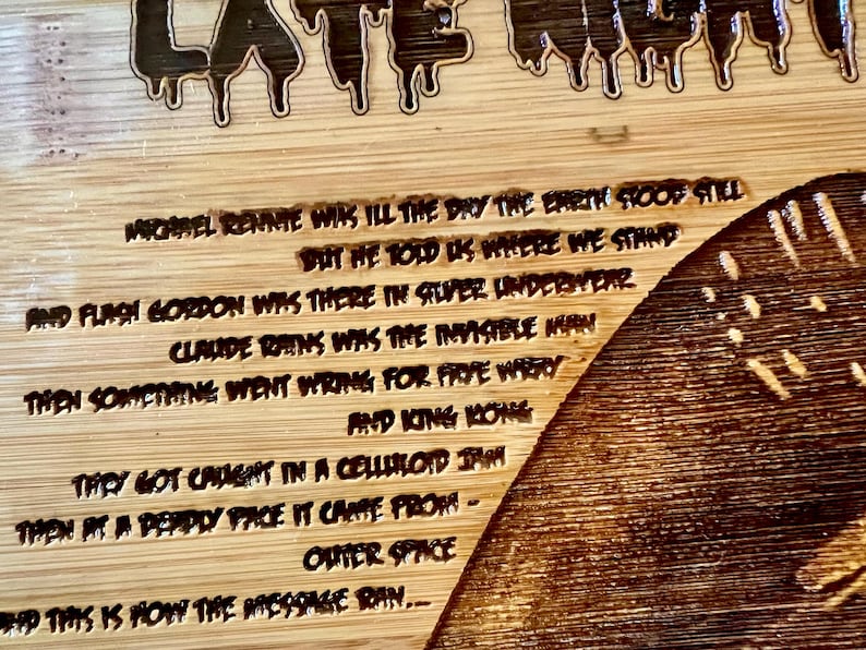 May include: A wooden cutting board with engraved text and a decorative design. The text includes phrases like "Late Night" and lines from a poem. The board has a natural wood grain.