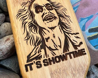 May include: A wooden paddle with a black and white image of a character from the movie "Beetlejuice" with the text "It's Showtime" engraved on the paddle.