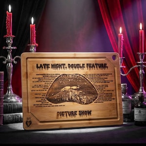 May include: A rectangular bamboo cutting board with the text "LATE NIGHT, DOUBLE FEATURE" and "PICTURE SHOW" engraved on it. The board features a detailed lip design and additional text. The scene includes candles, skulls, and bottles.