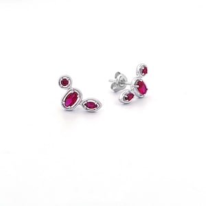 May include: A pair of silver earrings with a cluster of red gemstones in a geometric design.