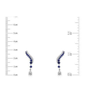 Puede incluir: Un par de pendientes plateados con un dise&ntilde;o curvo. Cada pendiente presenta una fila de piedras preciosas azules y un colgante en forma de l&aacute;grima. Los pendientes miden aproximadamente 2.5 cm de largo.