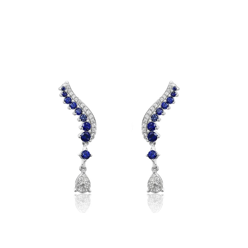 Puede incluir: Un par de pendientes plateados con un dise&ntilde;o curvo. Los pendientes presentan una serie de peque&ntilde;as piedras preciosas redondas de color azul oscuro y piedras claras y brillantes. Cada pendiente tiene un colgante en forma de l&aacute;grima en la parte inferior.