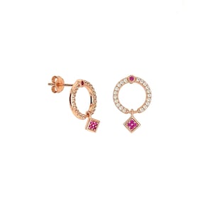 May include: A pair of rose gold earrings with a circle design. Each earring has a small square charm hanging from the bottom. The circle is set with small clear stones and the charm is set with pink stones.