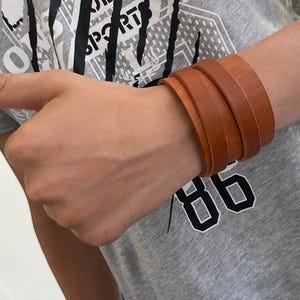May include: A brown leather bracelet with multiple layers. The bracelet is worn on a person's wrist.