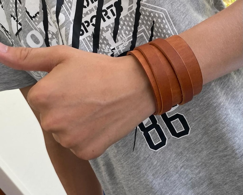 May include: A brown leather bracelet with multiple layers. The bracelet is worn on a person's wrist.