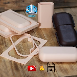 Könnte beinhalten: Eine Sammlung von hellpfirsichfarbenen, 3D-gedruckten Kunststoffformen und Schablonen für die Lederbearbeitung, darunter ein rechteckiges Gehäuse, ein hoher Zylinder und flache Rahmen mit Stichlochführungen sowie ein dunkelbraunes Lederetui.