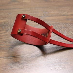 May include: A red leather cuff bracelet with two straps and silver metal rivets.