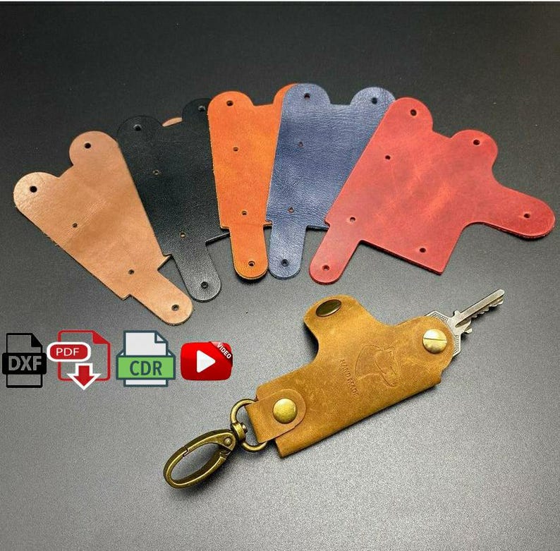 May include: Five leather keychains in different colors: brown, black, red, blue, and tan. The keychains are shaped like a small pocket. A tan leather keychain with a metal key ring and a silver key is attached to the keychain.