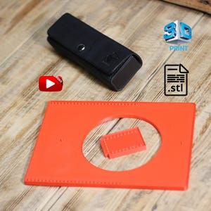 Könnte beinhalten: Ein schwarzes Lederetui mit Druckknopfverschluss und einem Pferdelogo, neben einem leuchtend orangefarbenen rechteckigen Objekt mit einem kreisförmigen Ausschnitt und einem kleinen orangefarbenen Stück. Das Bild enthält auch ein 3D-Druck-Logo, ein .stl-Dateisymbol und eine Video-Play-Schaltfläche.