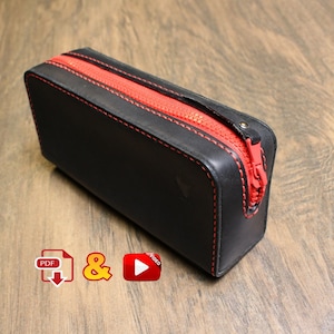 May include: Black leather zippered pouch with red stitching and a red zipper. The pouch is on a wood surface.