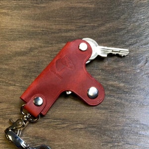 May include: Red leather key holder with a silver key and a silver chain. The key holder has a small animal silhouette and the words "HAND MADE" embossed on it.