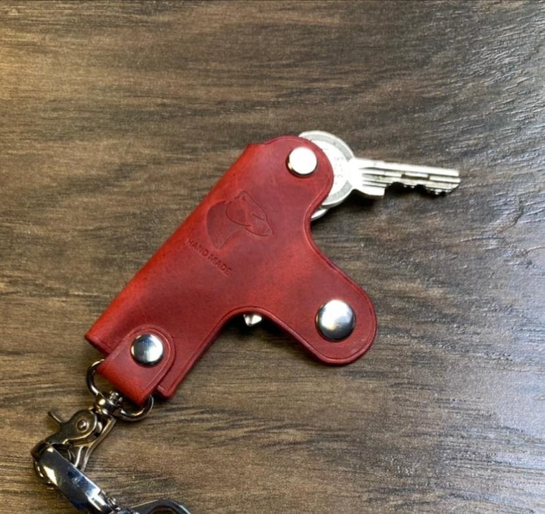May include: Red leather key holder with a silver key and a silver chain. The key holder has a small animal silhouette and the words "HAND MADE" embossed on it.