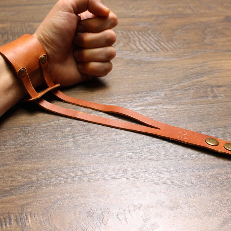 May include: A brown leather wrist strap with two adjustable straps and brass accents. The strap is worn on a person's wrist.