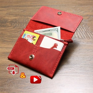 May include: Red leather wallet with a zipper closure, open to reveal two card slots and a cash pocket. The wallet is on a wooden surface.