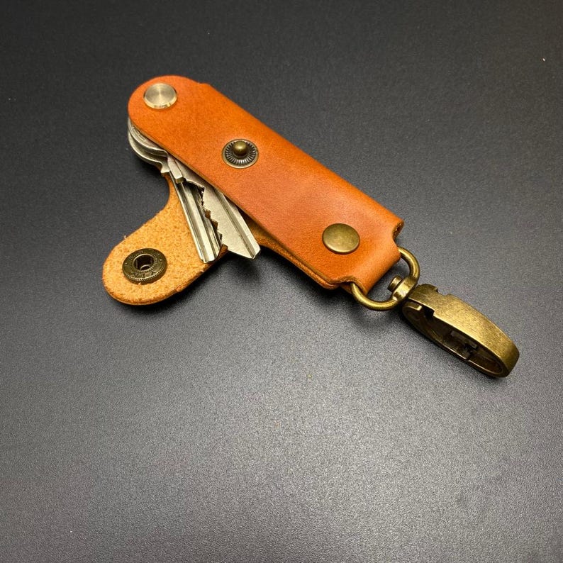May include: A brown leather key holder with a metal clasp and three keys. The holder has two brass rivets and a brass button.