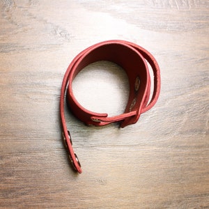 May include: A red leather bracelet with gold-toned metal snaps.