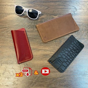 May include: Three different leather eyeglass cases. One is brown, one is red, and one is black with a crocodile pattern. The cases are all stitched with yellow thread. The image also includes a pair of white sunglasses and a download icon.