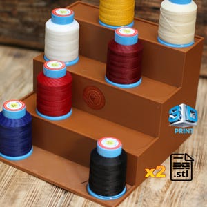 May include: A brown tiered display stand holding spools of thread in various colors, including white, red, blue, black, and yellow. The spools have blue and yellow accents. The stand has a 3D print logo and the text "PRINT".