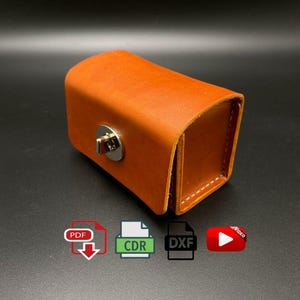 Könnte beinhalten: Ein rechteckiges, orangefarbenes Lederetui mit einem silbernen Verschluss. Das Etui ist mit weißem Faden genäht und hat eine gewölbte Oberseite. Symbole für PDF, CDR, DXF und ein Video befinden sich im unteren Teil des Bildes.