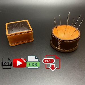 Könnte beinhalten: Zwei Leder-Nähkissen, eines quadratisch und eines rund, mit braunem Leder und orangefarbenen Nähten. Das runde Nähkissen hat mehrere Nadeln, die herausragen. Das Bild enthält auch Symbole für herunterladbare Dateien in den Formaten PDF, DXF und CDR sowie ein Wiedergabesymbol für ein Video-Tutorial.