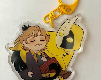 May include: A yellow and black cartoon character with a crown and a mustache is sitting on a yellow and black bird with wings. The character is wearing a purple coat, red and white striped pants, and brown shoes. The character has its eyes closed and is sleeping. The character and bird are on a clear acrylic keychain with a yellow metal ring.