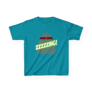 May include: A turquoise t-shirt featuring a gray shape with a red stripe and a red dot. The word "ZZZZZING!" is written in a neon green font across the design. The shirt is made of a soft material.