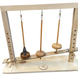 Può includere: Un giocattolo di equilibrio in legno con tre fusi sospesi. I fusi hanno forme diverse: un cono, un disco e un cilindro. Il telaio è in legno chiaro e ha supporti regolabili.