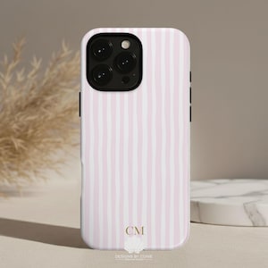 May include: A phone case with a pink and white striped pattern. The case has a black camera module and black side buttons. The bottom of the case has the initials "CM" and the text "DESIGNS BY CONIE GRAPHIC STUDIO".