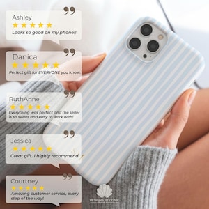 May include: A light blue and white striped phone case. The case is held in a person's hand. The image includes customer reviews with text such as "Looks so good on my phone!!" and "Great gift. I highly recommend."