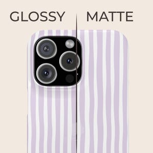 May include: A phone case with a vertical striped pattern in white and light purple. The text "GLOSSY" and "MATTE" are displayed above the phone case. The phone case has a camera module with three lenses and a flash.