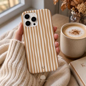 May include: A phone case featuring a pattern of vertical, hand-drawn style tan and white stripes. The case has a cutout for a triple-lens camera system and the initials SJ printed in a small, dark font near the bottom center of the back panel.