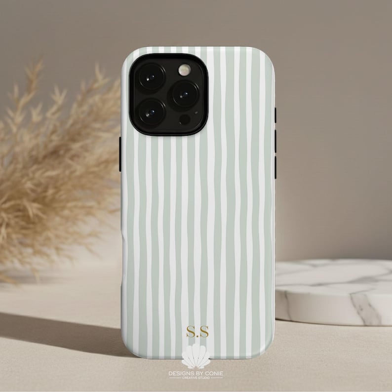 May include: A phone case with a vertical striped pattern in light green and white. The case has a black camera module and side buttons. The bottom of the case features the initials "S.S" and the text "DESIGNS BY CONIE".